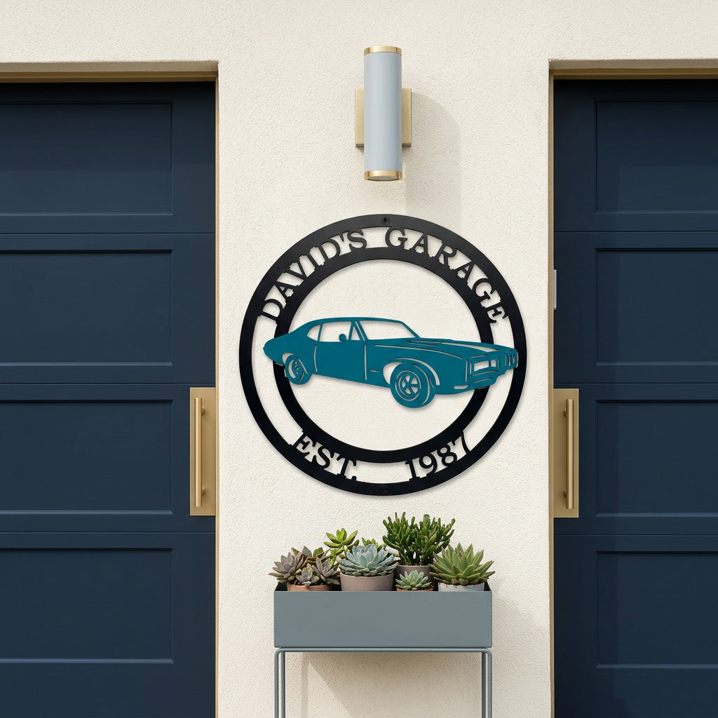 Custom metal garage sign featuring classic car silhouette with personalized garage name and established year mounted between modern blue garage doors with succulent planter below