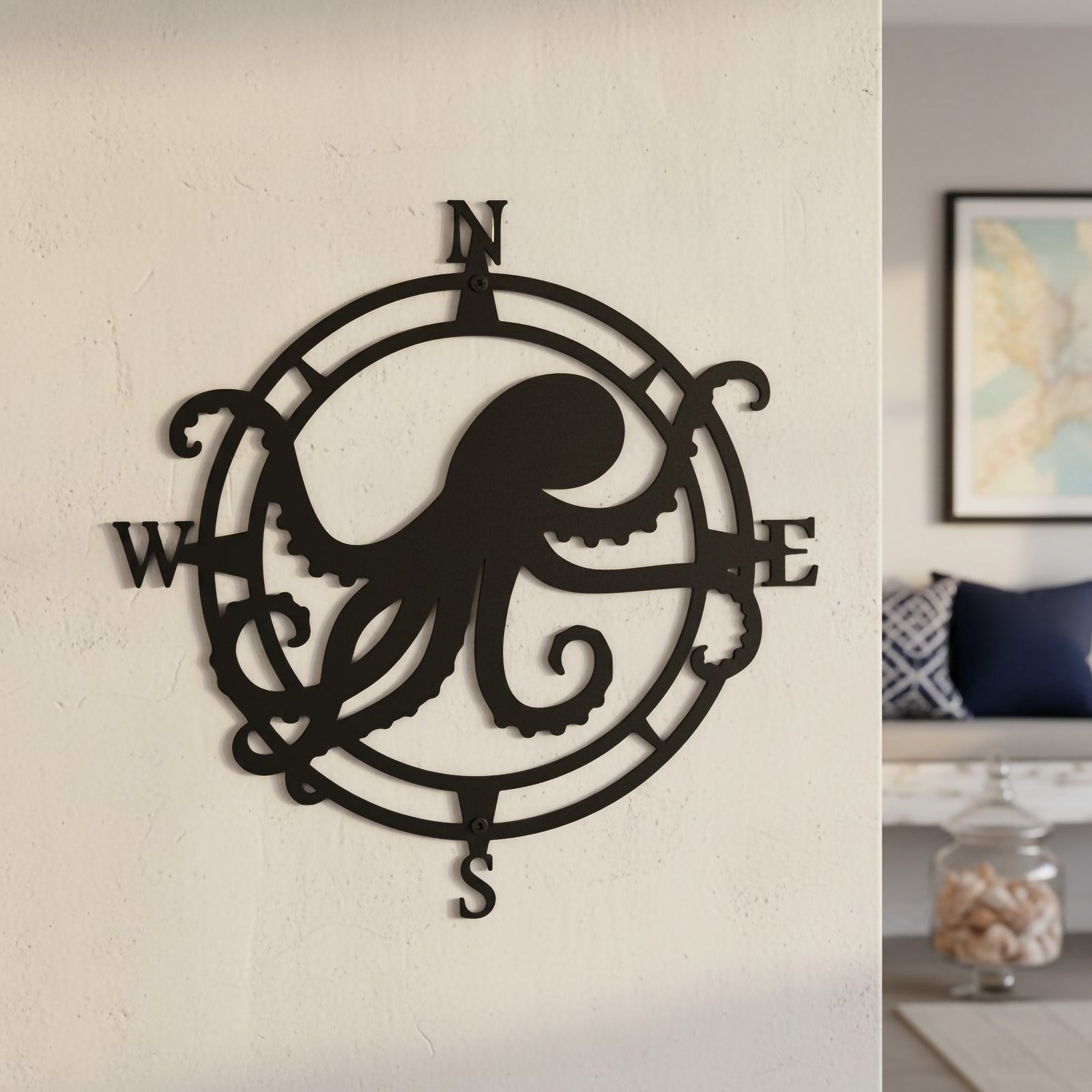 Elegant satin black custom circular octopus compass sign styled on an interior wall looking into a coastal living space with blue accent cushions.