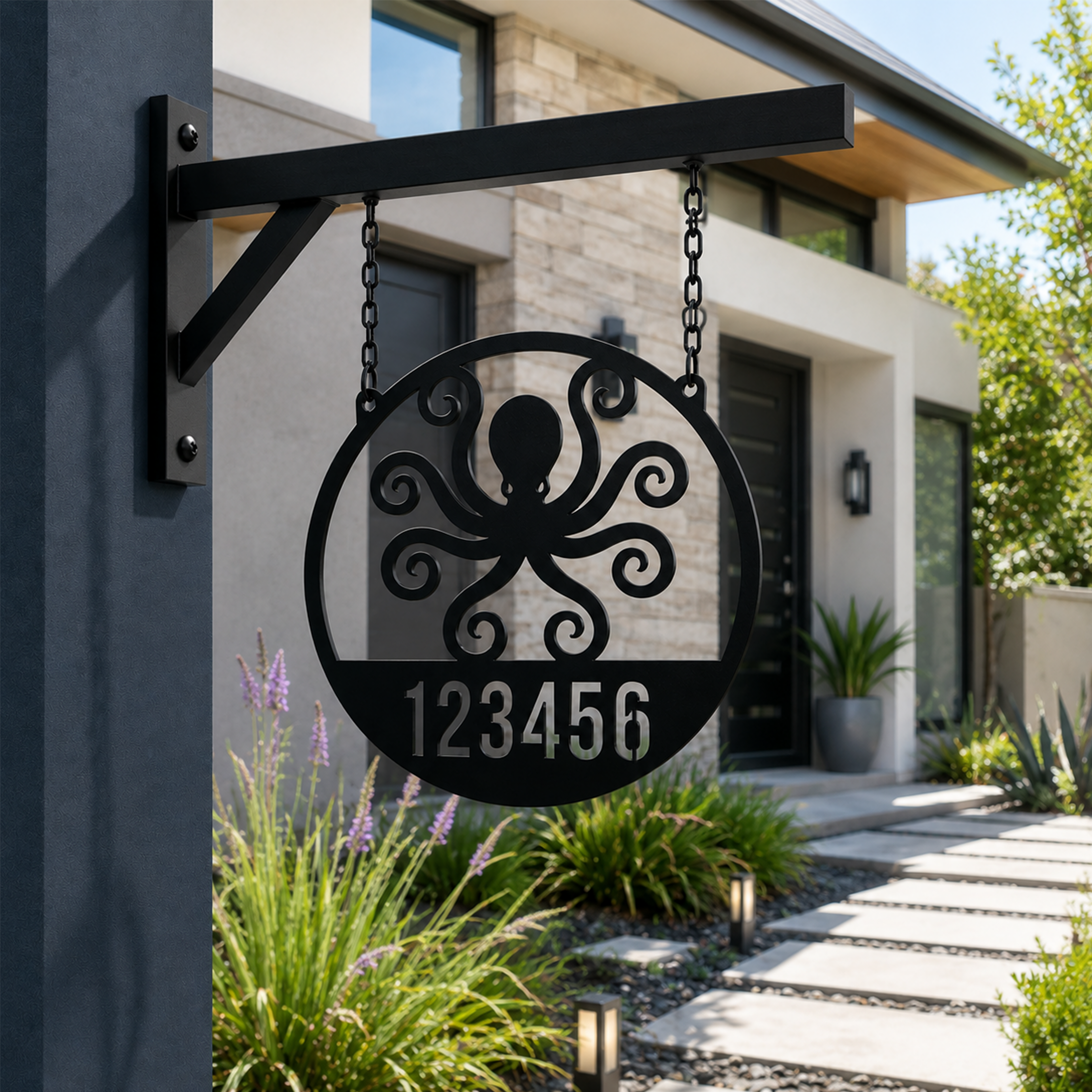 A circular matte black metal address sign featuring a laser-cut octopus motif above the numbers "123456". The sign hangs from short chains attached to a black metal wall bracket mounted on a dark grey stucco pillar, showcasing a concrete walkway and landscaped front yard in the background.