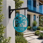 A circular custom metal house sign in a vibrant turquoise finish, highlighting a laser-cut octopus shape and the custom text "123456". The piece hangs from chains on a black metal post attached to a textured white stucco entry wall of a contemporary home.