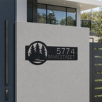 Black personalized metal house number plaque with pine tree artwork mounted beside modern home entrance displaying 5774 Main Street