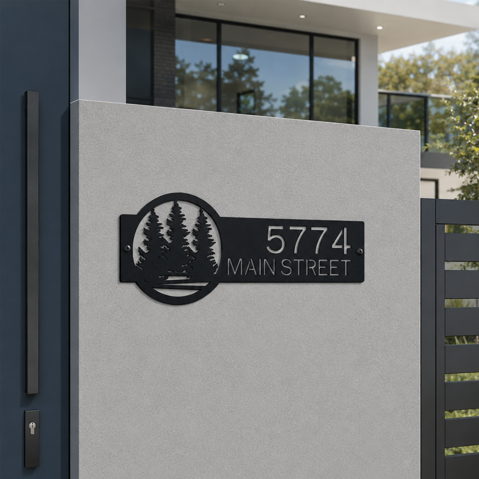 Black personalized metal house number plaque with pine tree artwork mounted beside modern home entrance displaying 5774 Main Street