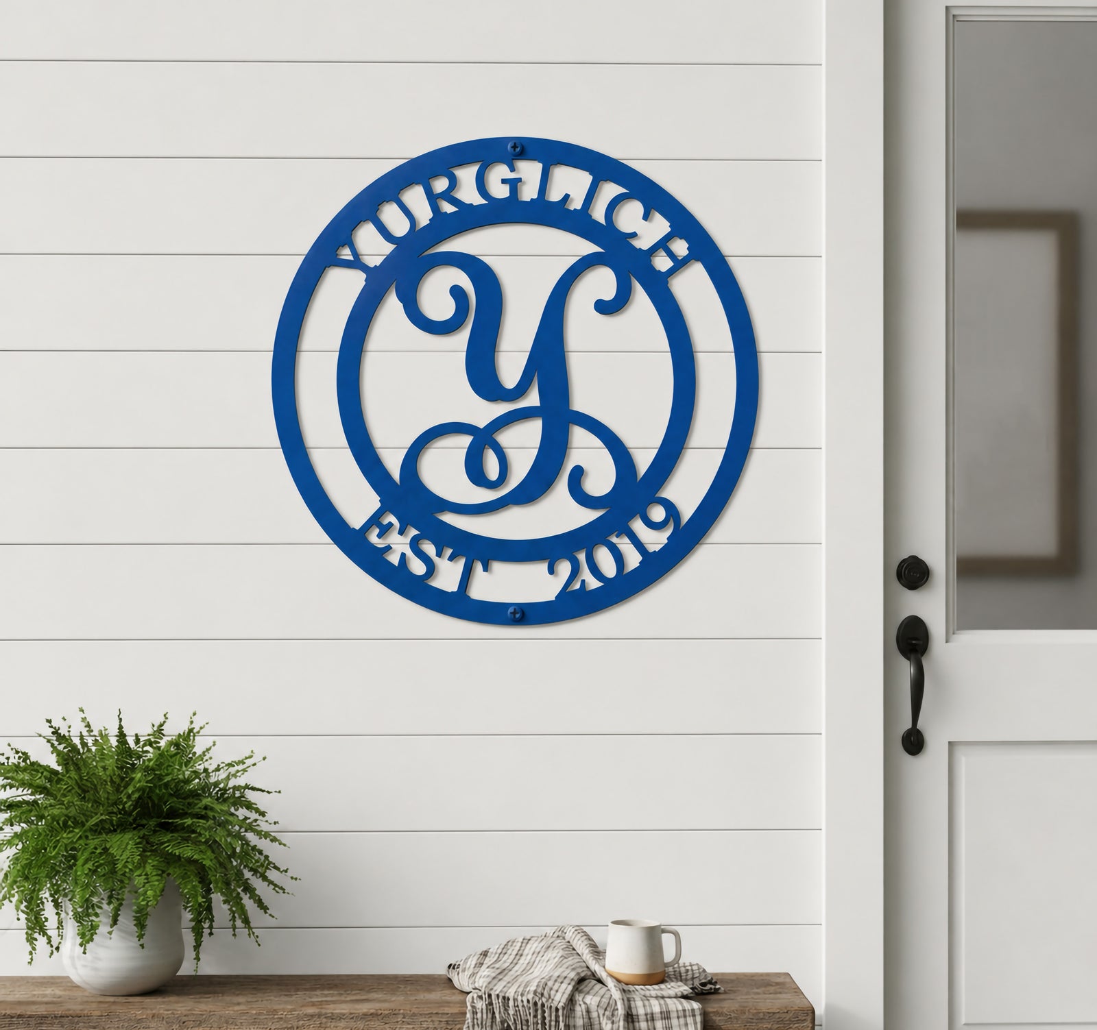 Panther blue custom metal initial monogram plaque displayed on a white shiplap outdoor wall above a wooden porch bench with cozy decor.