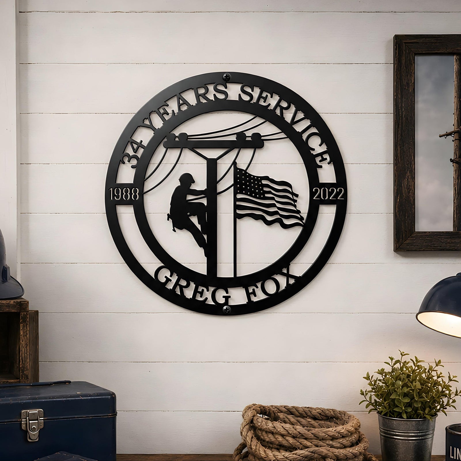 Black custom lineman years of service metal sign displayed in workshop with helmet gloves rope and tools