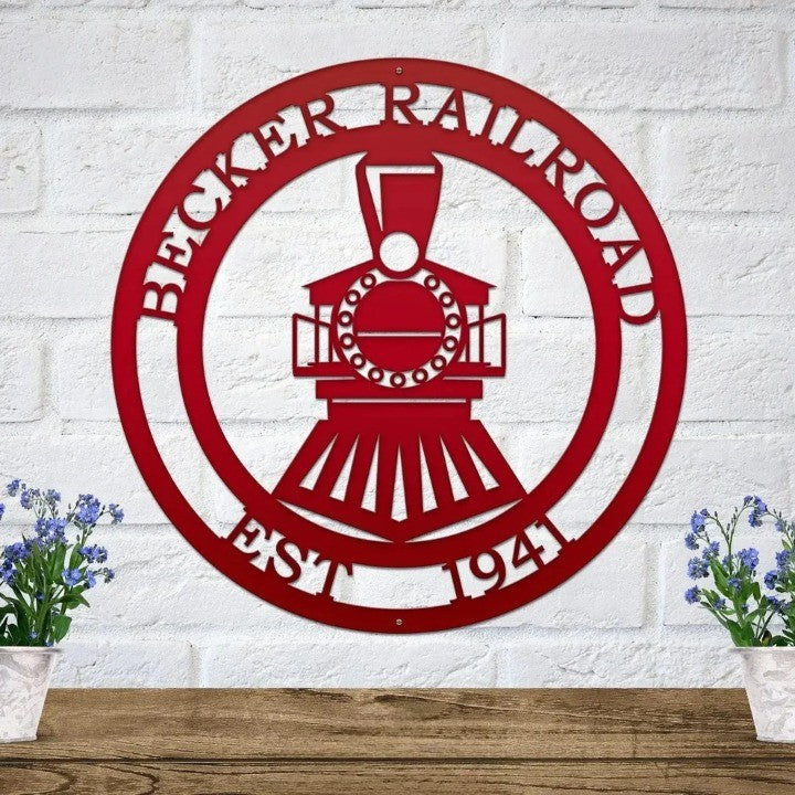 Red metal steam train sign with custom name and date on white brick above a wooden shelf with blue potted flowers.