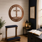 A metallic rose gold circular metal sign displaying the custom text "JOE & STEPHANIE" and "JOHN 3:16" is hung in a prayer room setting. The sign is mounted on white wood paneling over a wooden kneeling bench, a side table with a lit candle lantern, and an open Bible resting on a nearby desk.