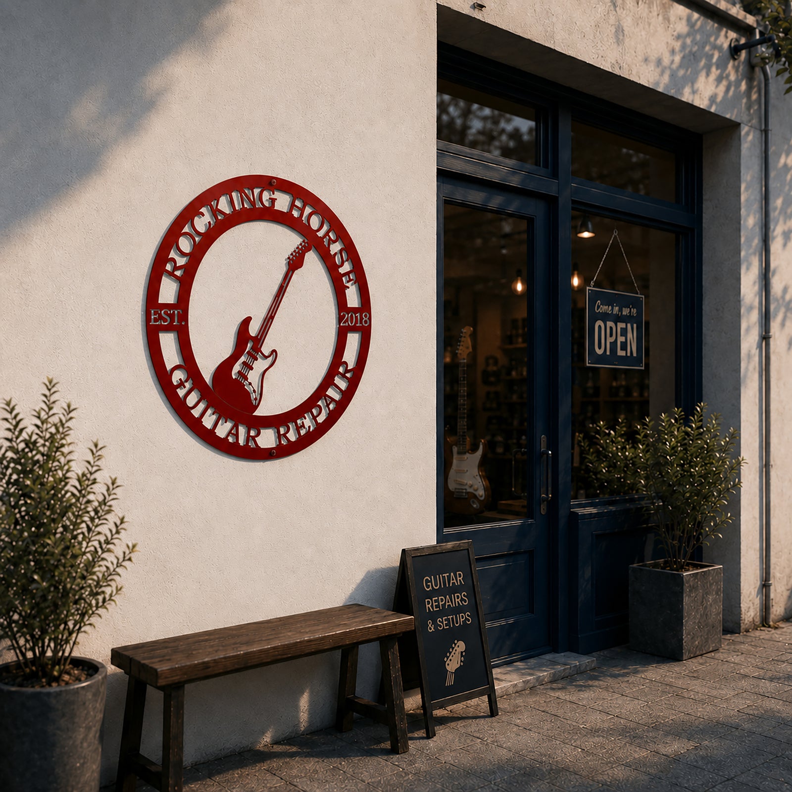 Deep red custom guitar repair metal sign mounted on the exterior white wall of a music store next to an open glass door and wooden bench.