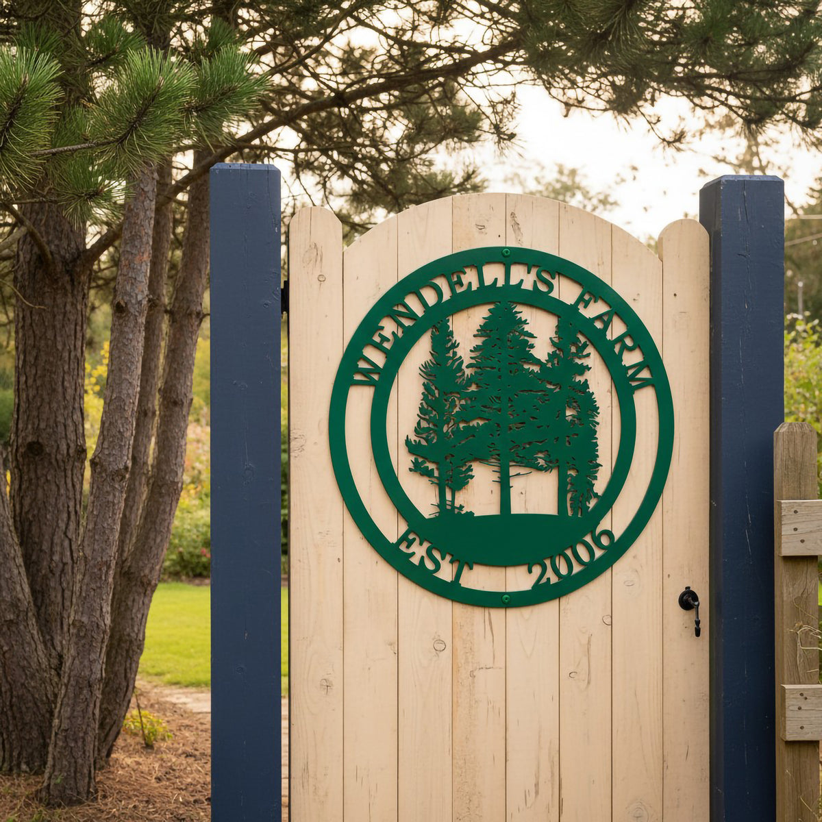 A green round metal farm sign reading "Wendell's Farm Est. 2006" fixed to a light wood arched gate supported by dark blue posts at a property entrance.