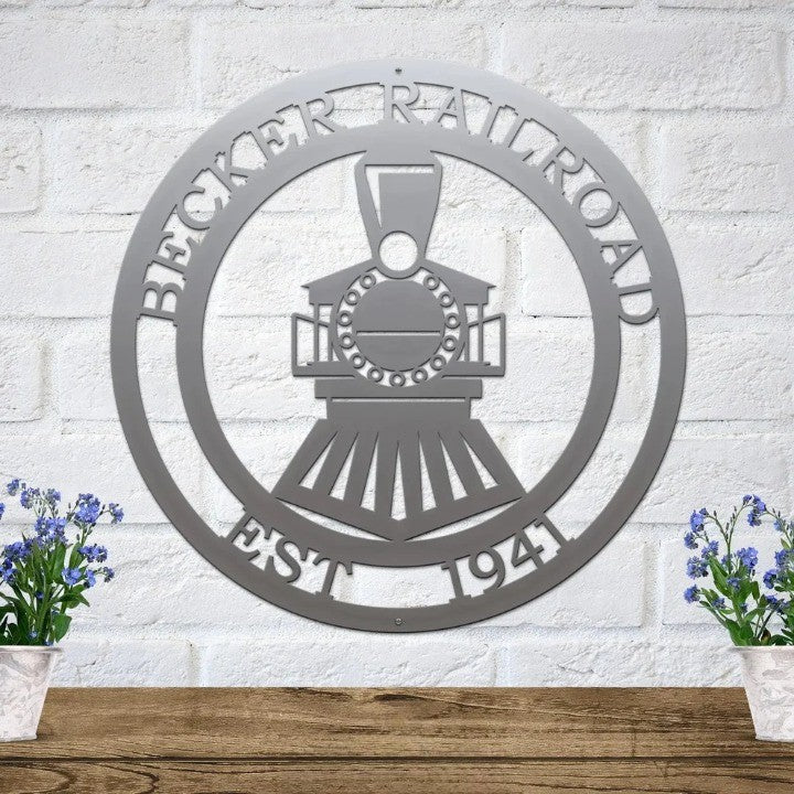 Silver metal train sign featuring custom text on a white brick wall above a rustic shelf with blue flowers in pots.