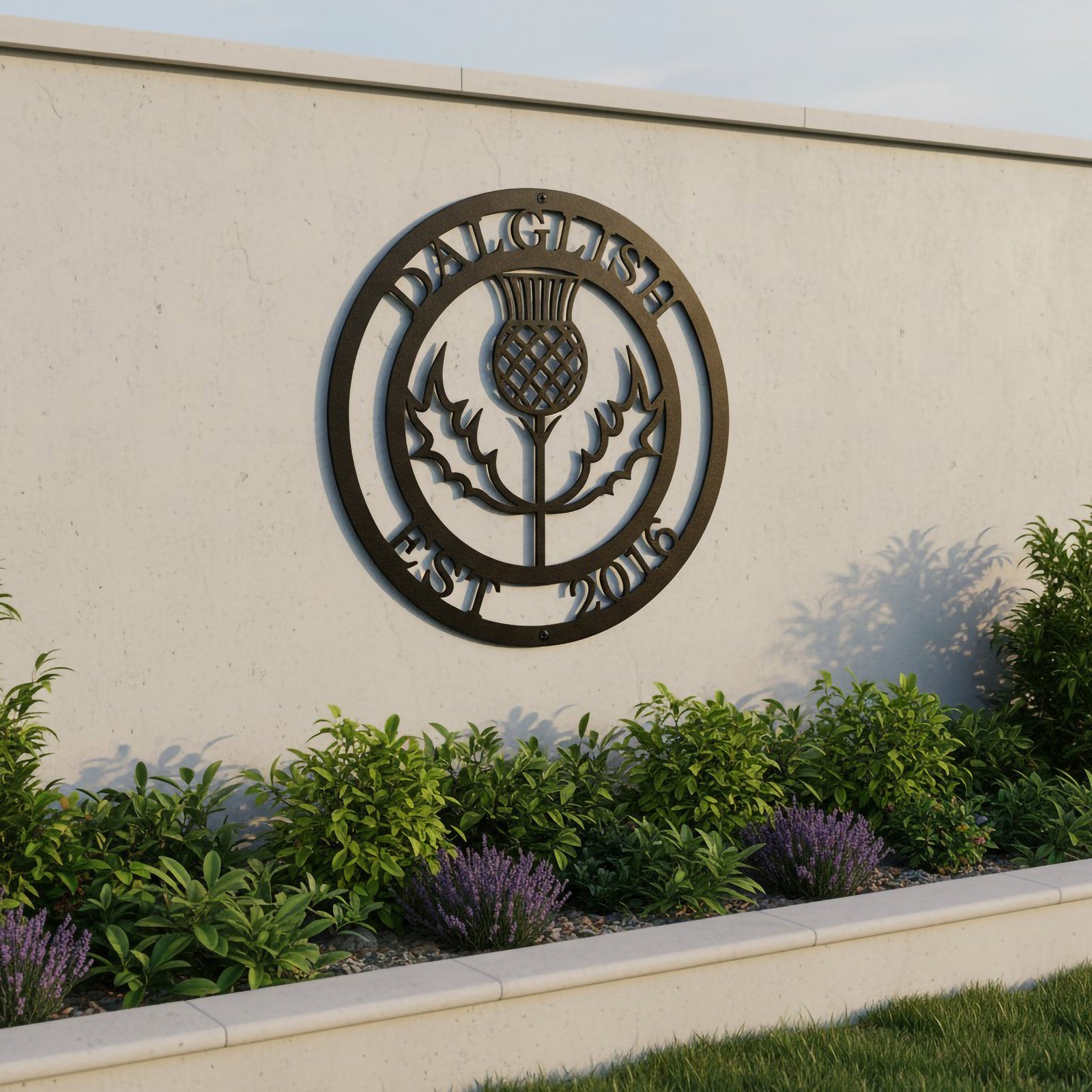Black bronze finished custom Scottish thistle metal emblem hanging on a modern white concrete garden wall above a flower bed of lavender.