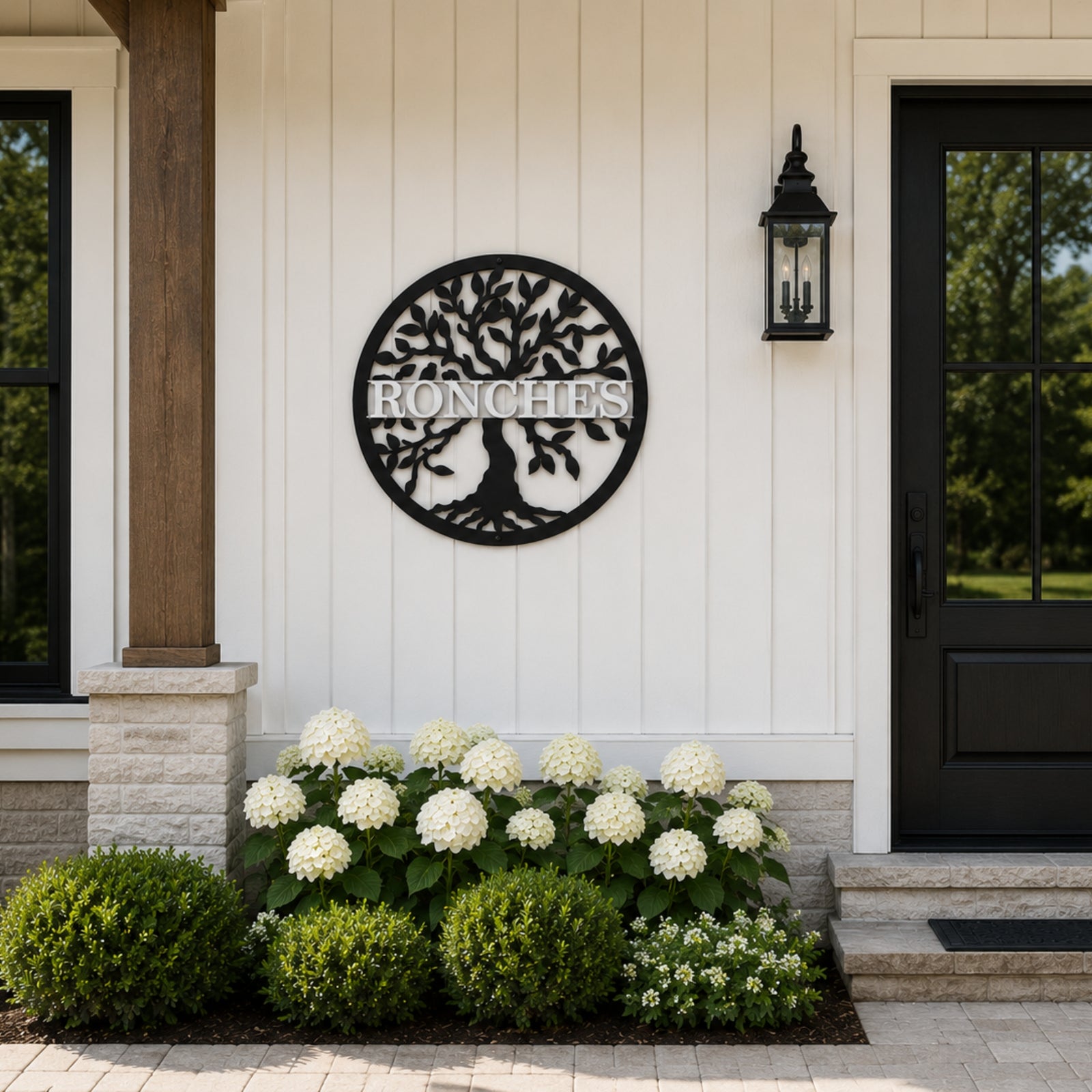 Custom tree of life metal family sign mounted on white farmhouse porch wall with flowers and black front door