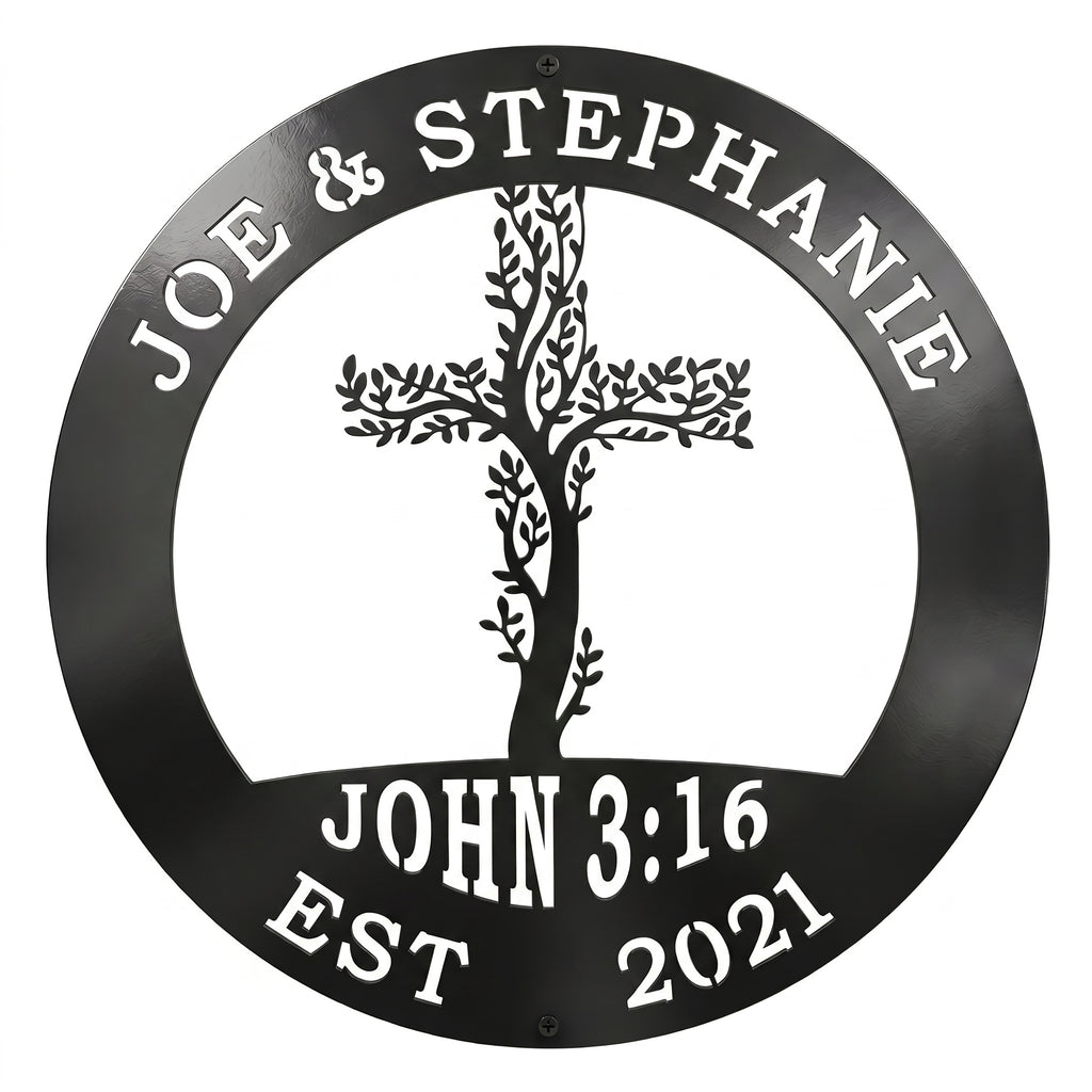 A circular metal sign finished in a glossy black color is displayed over a solid white background. The top rim is cut out with the names "JOE & STEPHANIE," the bottom features "JOHN 3:16 EST 2021," and the center showcases an intricate cross woven with climbing tree branches and leaves.