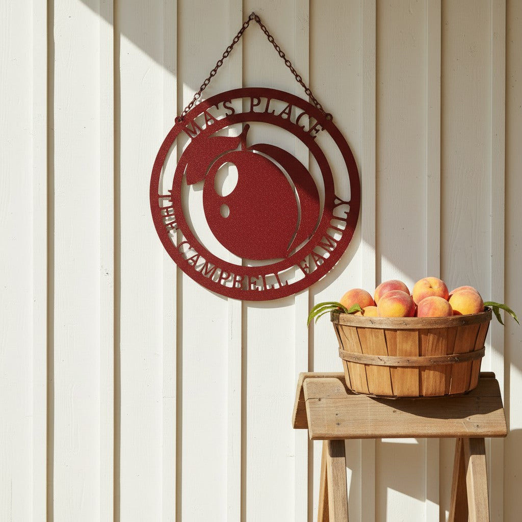 Red personalized hanging metal peach sign reading "Ma's Place The Campbell Family", mounted on white vertical siding next to a basket of fresh peaches on a wooden stool.
