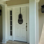 Black pineapple welcome metal door hanger displayed on white front door for inviting porch entry decor
