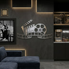 Polished chrome film reel and clapperboard wall sign mounted on a dark cinema room wall