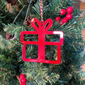 Red gift-shaped ornament hanging on Christmas tree with green leaves and red berries, festive holiday decoration for seasonal décor and Christmas tree display
