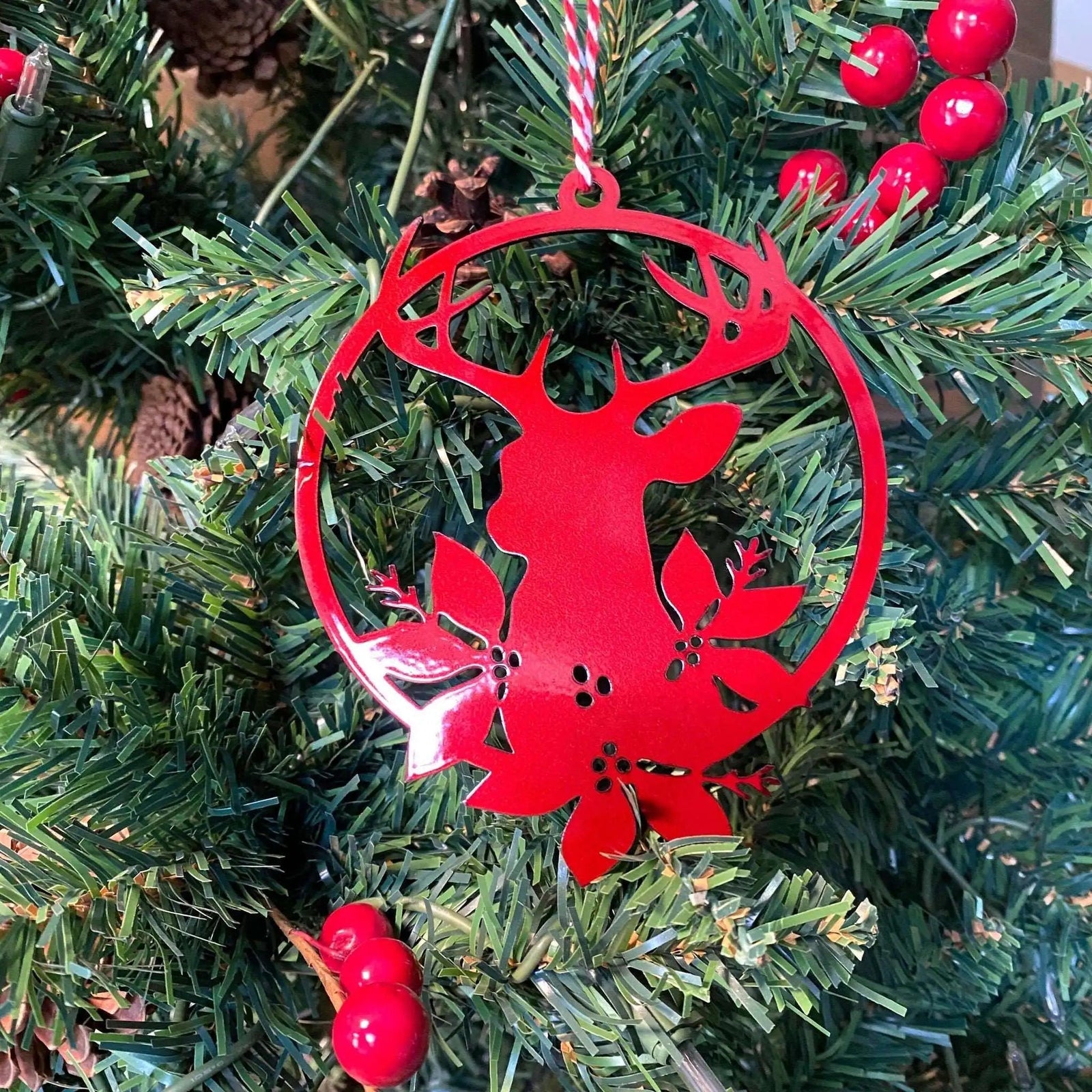Red metal reindeer Christmas ornament hanging on festive holiday tree with berries and pinecones