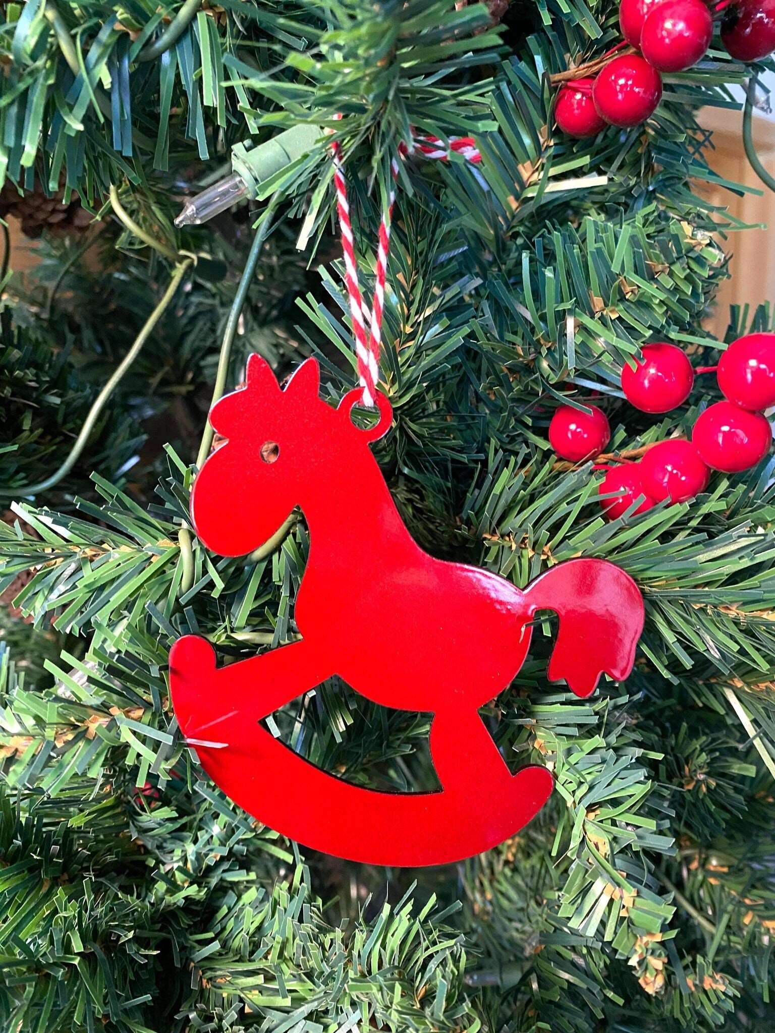 Red rocking horse metal Christmas ornament displayed on green Christmas tree branches