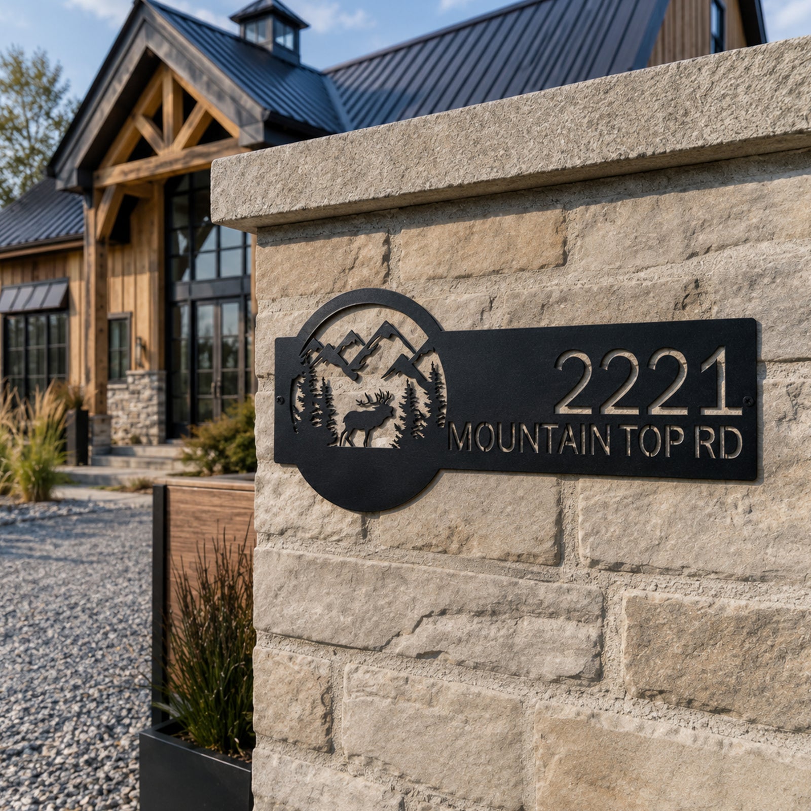 Black metal elk mountain address sign displayed on stone gate column in front of modern rustic cabin home