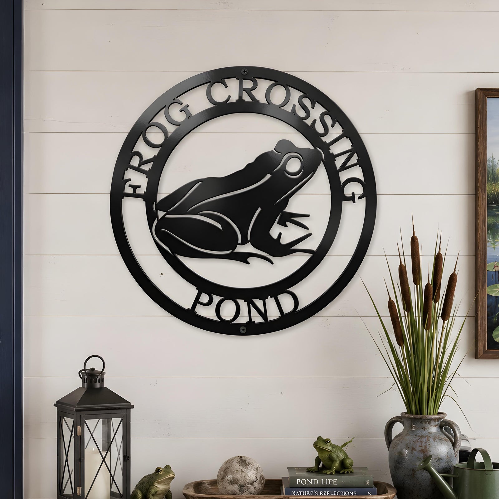 Black frog pond metal wall art displayed above rustic console table with lanterns and pond themed decor