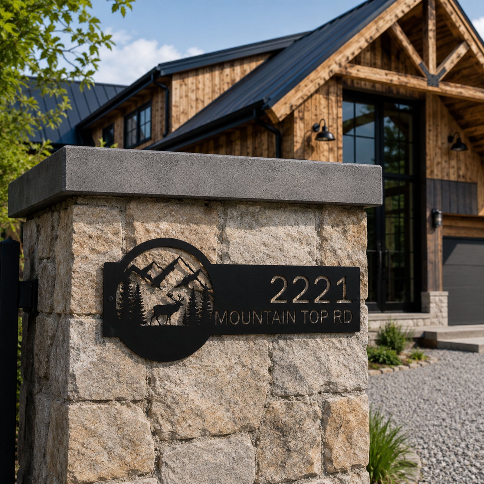 Black custom metal house address sign featuring elk forest and mountain scene mounted on stone pillar outside rustic lodge home