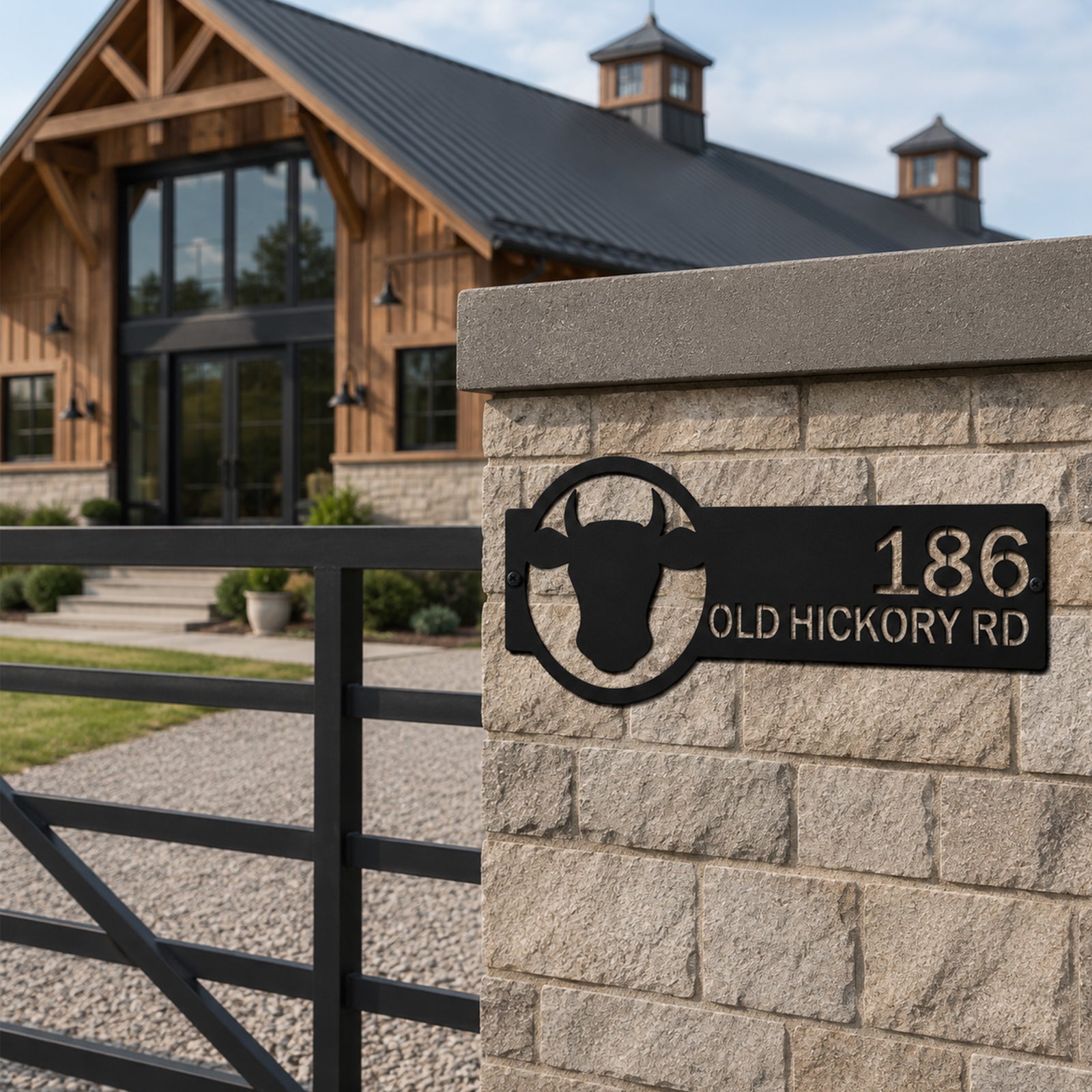 Black ranch style metal address sign with bull silhouette and custom house number mounted on stone gate pillar