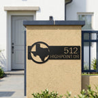 Black personalized Texas address plaque mounted on outdoor stucco gate pillar with modern home background