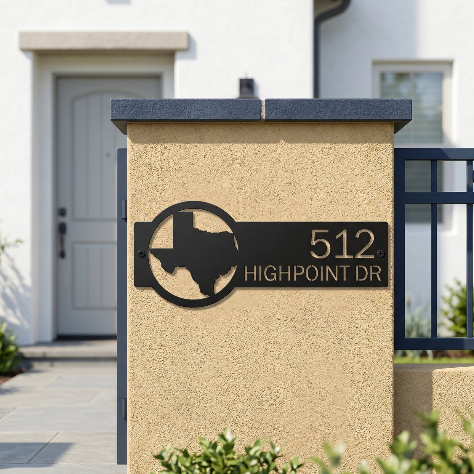 Black personalized Texas address plaque mounted on outdoor stucco gate pillar with modern home background