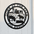 Black down at the farm metal sign with pigs and barn scene mounted near an outdoor pig enclosure