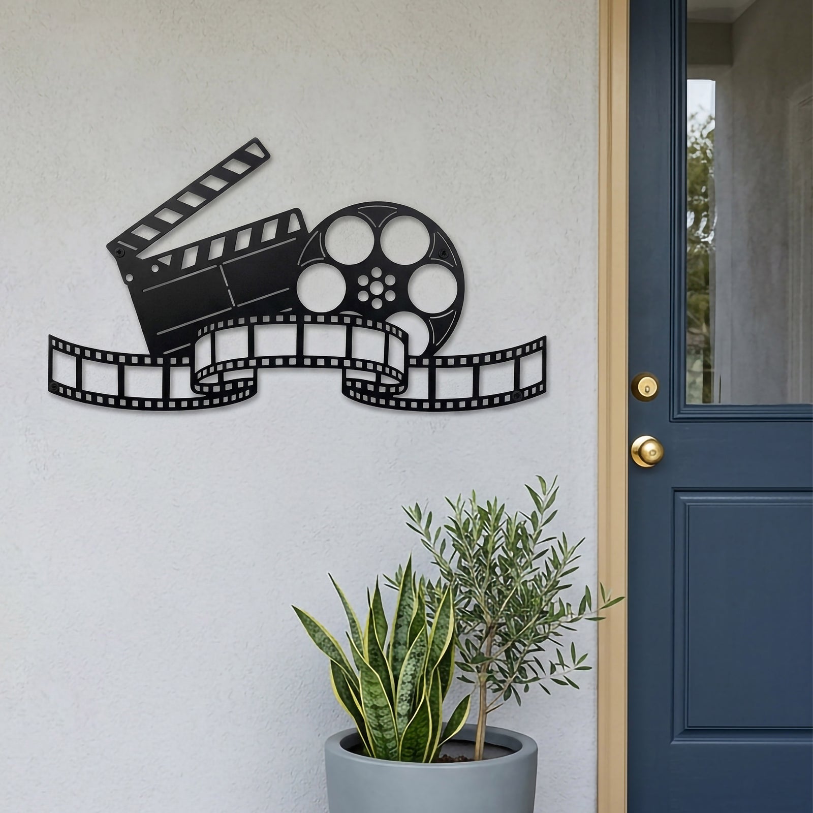 Satin black movie reel and clapperboard metal wall decor mounted beside a blue entry door with modern potted plants and film strip design