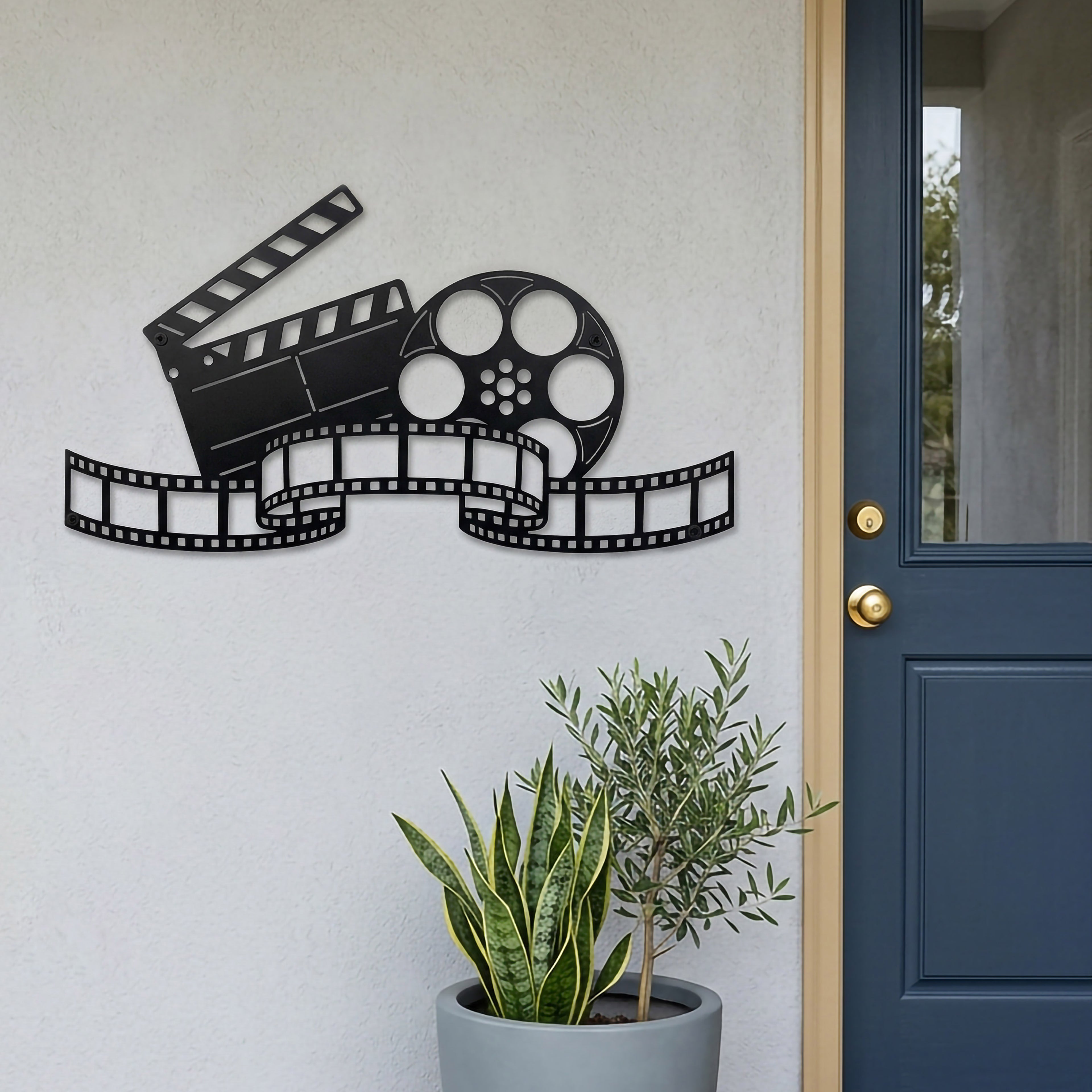 Satin black movie reel and clapperboard metal wall decor mounted beside a blue entry door with modern potted plants and film strip design