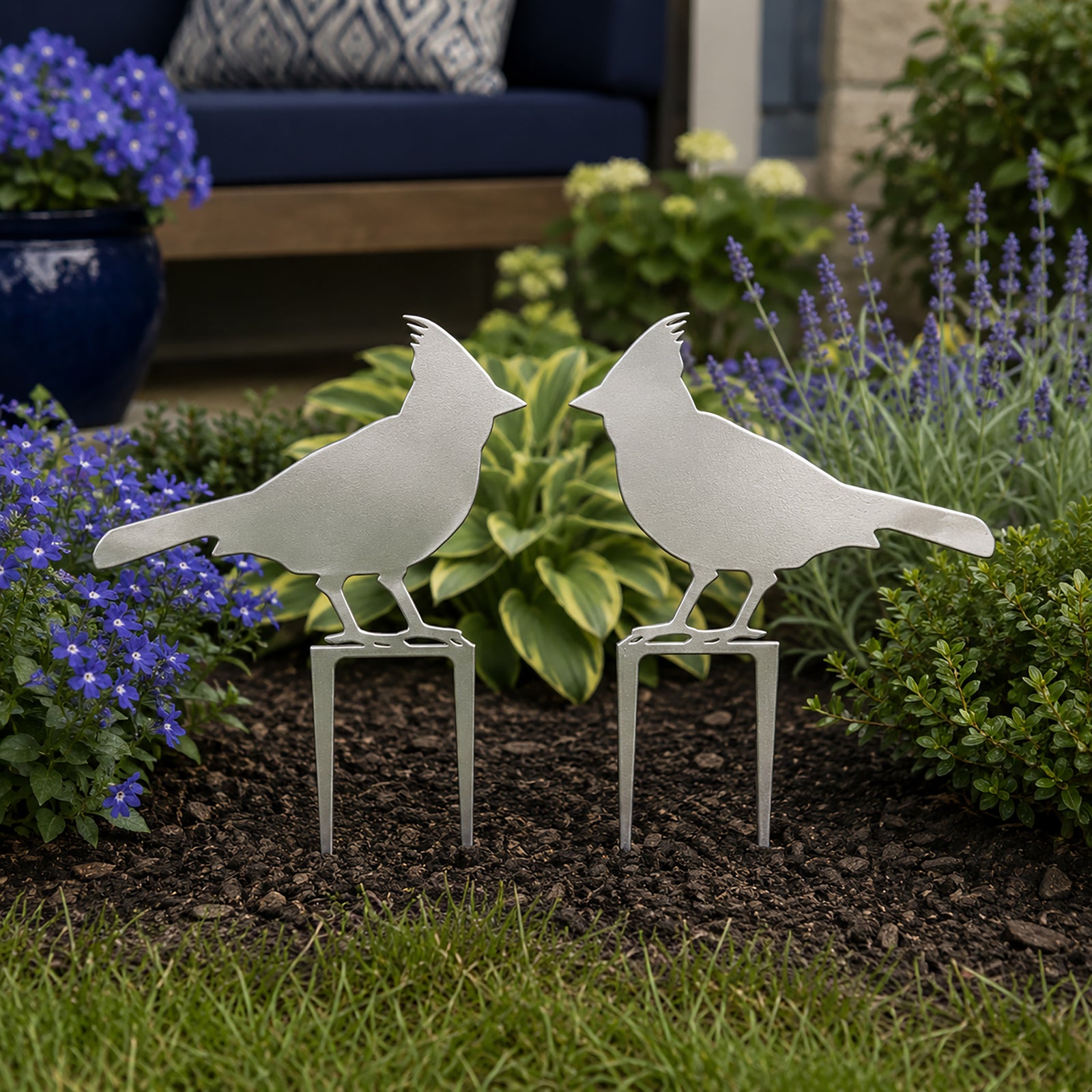 Satin titanium cardinal metal garden stakes placed in a landscaped flower bed with purple blooms and greenery