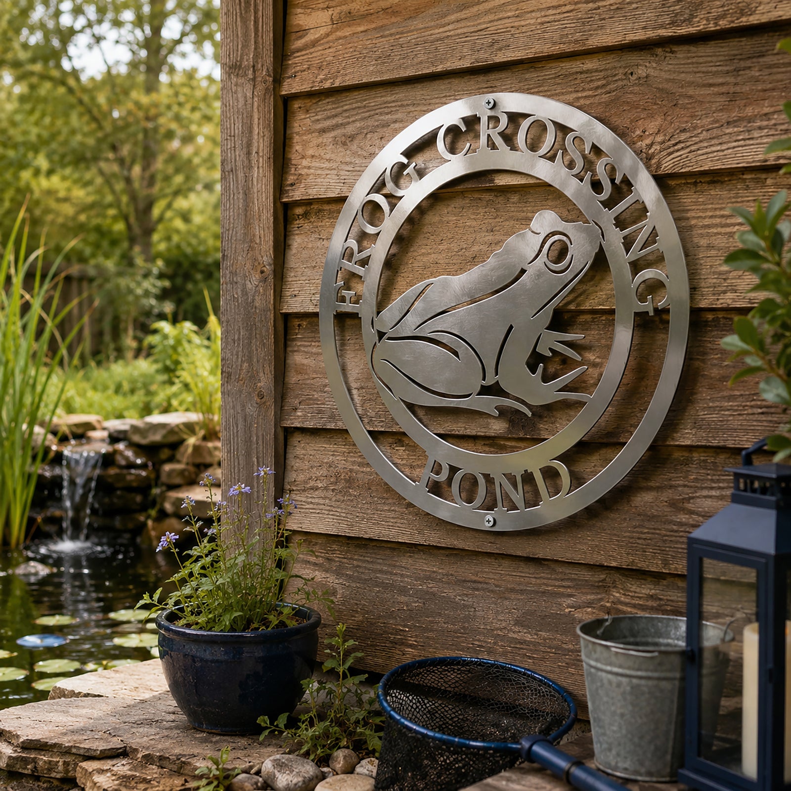 Satin titanium frog crossing pond metal wall sign displayed beside outdoor garden pond and wooden cabin wall