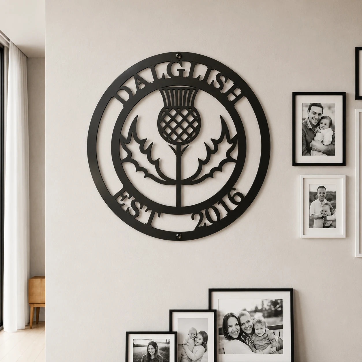 A circular black metal wall sign featuring a thistle and the text 'DALGLISH EST 2016' mounted on a beige wall, with several framed black-and-white family photos displayed nearby.