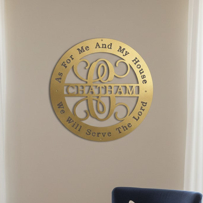 A circular metal cutout sign in a matte gold finish featuring the name "CHATHAM" and the text "As For Me And My House We Will Serve The Lord." It is displayed on a plain taupe living room wall with the top of a navy blue armchair visible at the bottom of the frame.