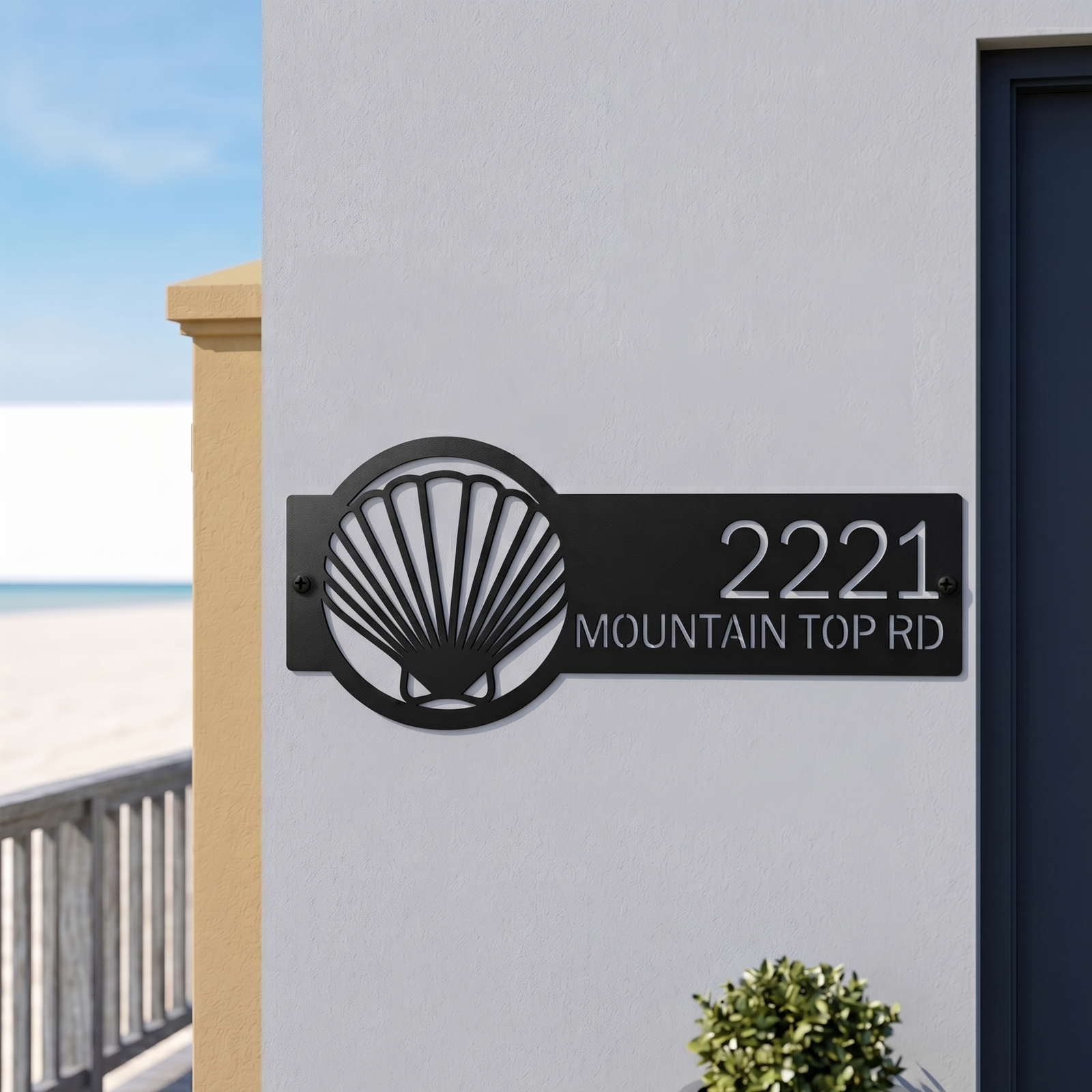 Black metal seashell address sign with house number on white wall near beach entrance