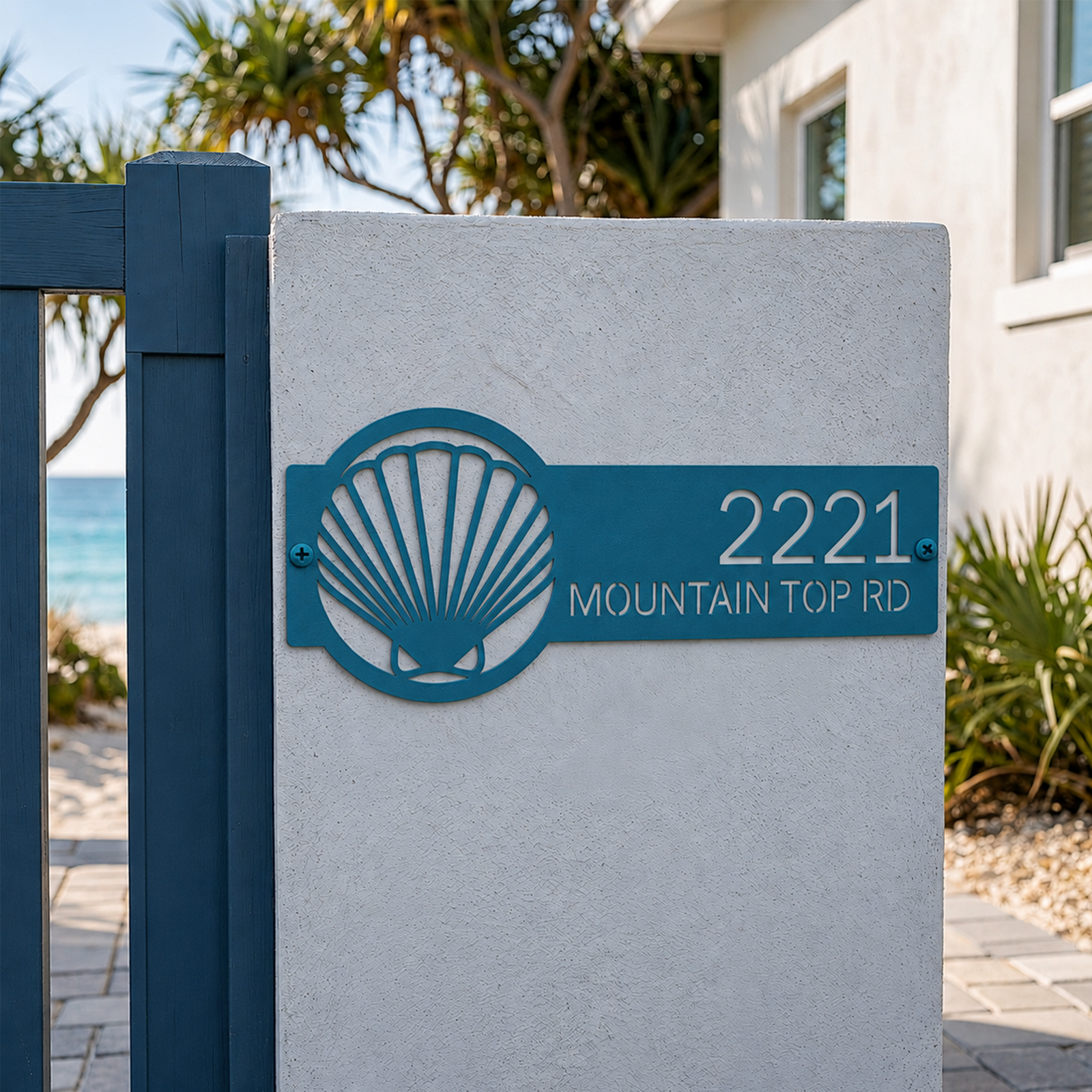 Turquoise seashell address plaque with house number on white coastal gate pillar