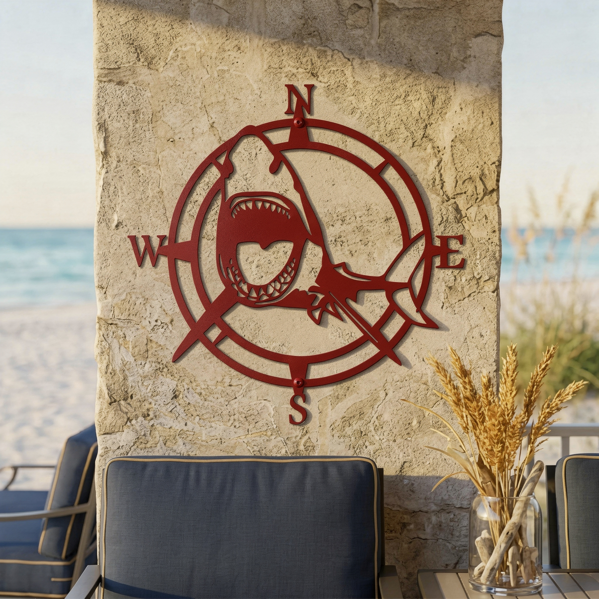 Deep red shark compass metal wall art displayed on a stone patio wall with beach seating and ocean view