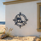 Navy blue shark compass metal wall art mounted on a beach house exterior wall with sand and ocean in the background