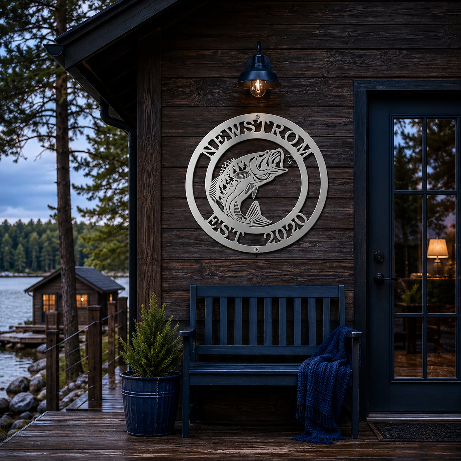 Silver bass fish metal sign with Newstrom and Est 2020 mounted on a dark wood cabin wall near a lakeside porch