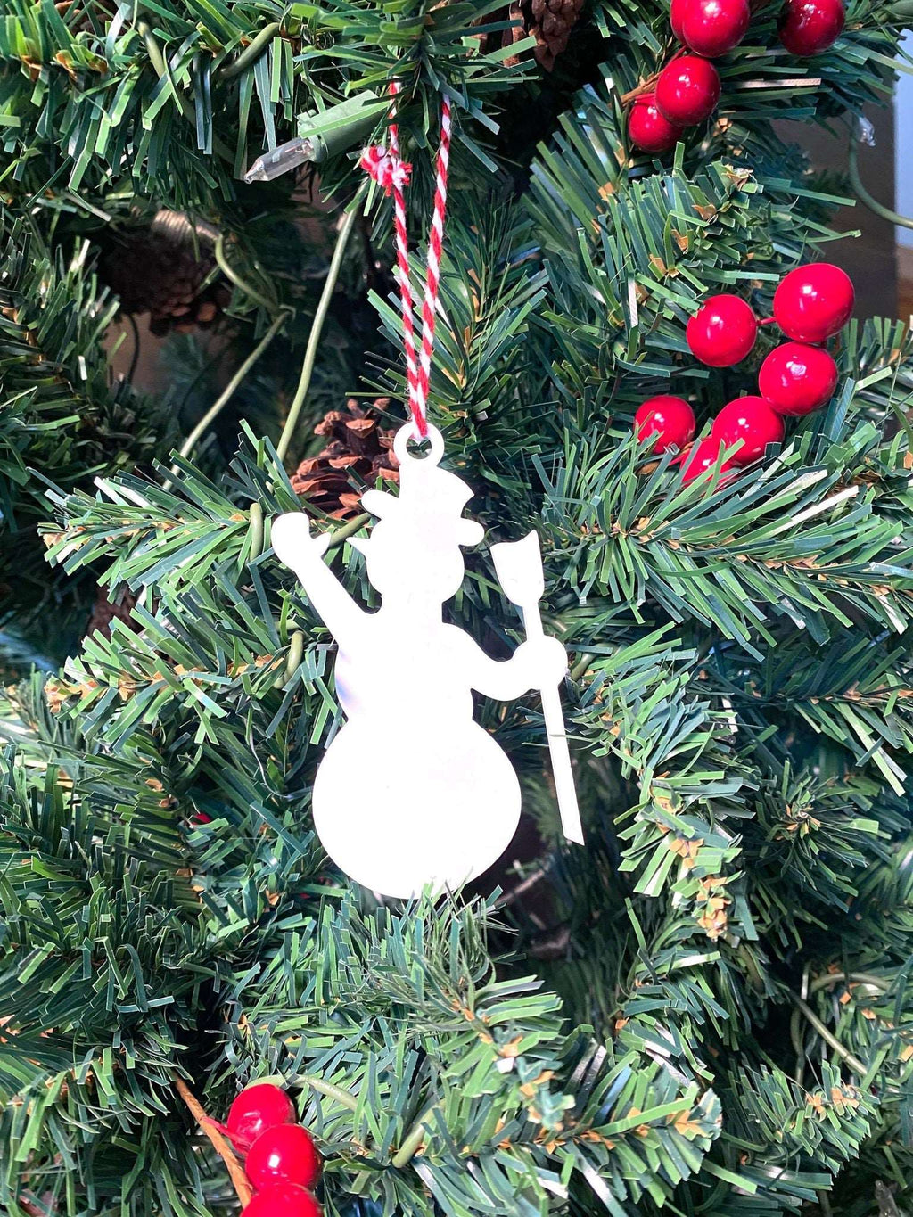 White snowman metal Christmas ornament hanging on decorated Christmas tree with red berry accents