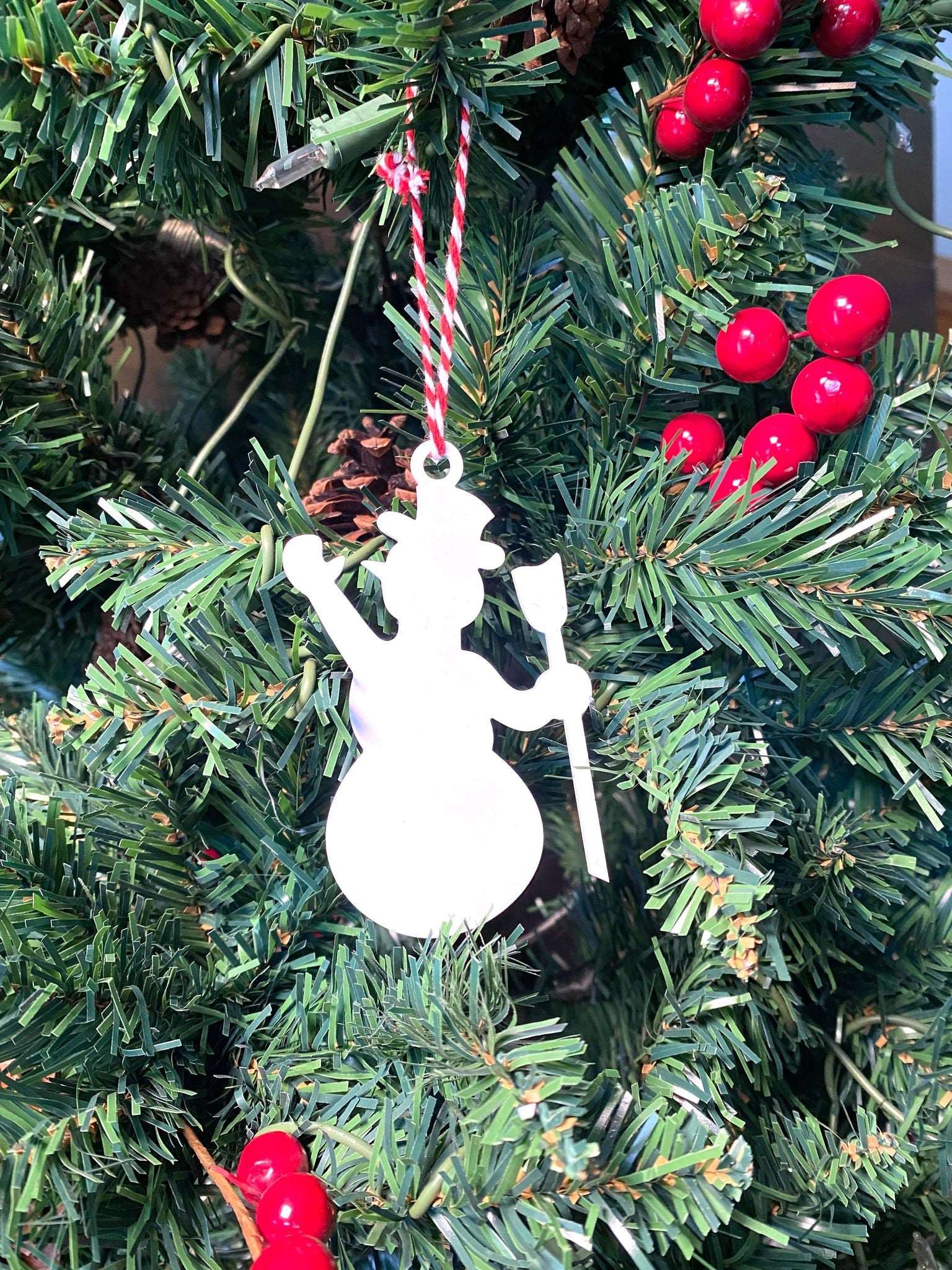 White snowman metal Christmas ornament hanging on decorated Christmas tree with red berry accents