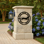 Black The Fox Den metal wall art with running fox design mounted on a stone pillar beside hydrangeas and outdoor pathway