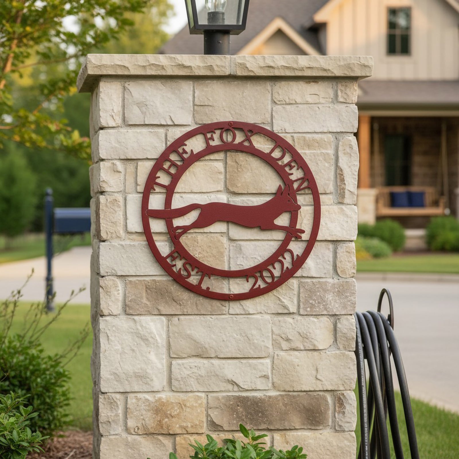 Deep red The Fox Den metal wall art with fox silhouette mounted on a stone outdoor pillar near a residential front yard