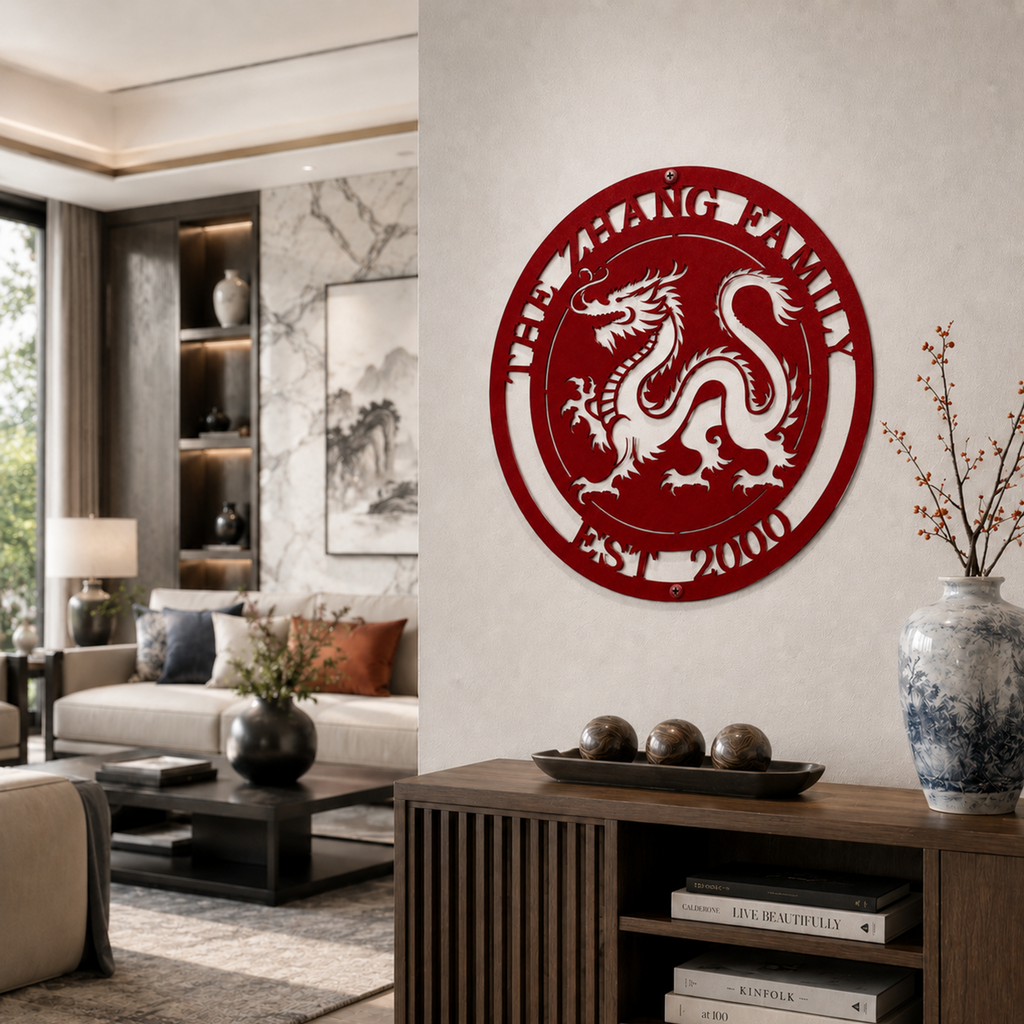A vibrant ruby red circular metal heritage plaque featuring an intricate traditional dragon centerpiece and the words "THE ZHANG FAMILY EST. 2000" cut out along the top and bottom arches. It is hung in a modern living room setting over a wooden cabinet styled with an Asian ceramic vase.