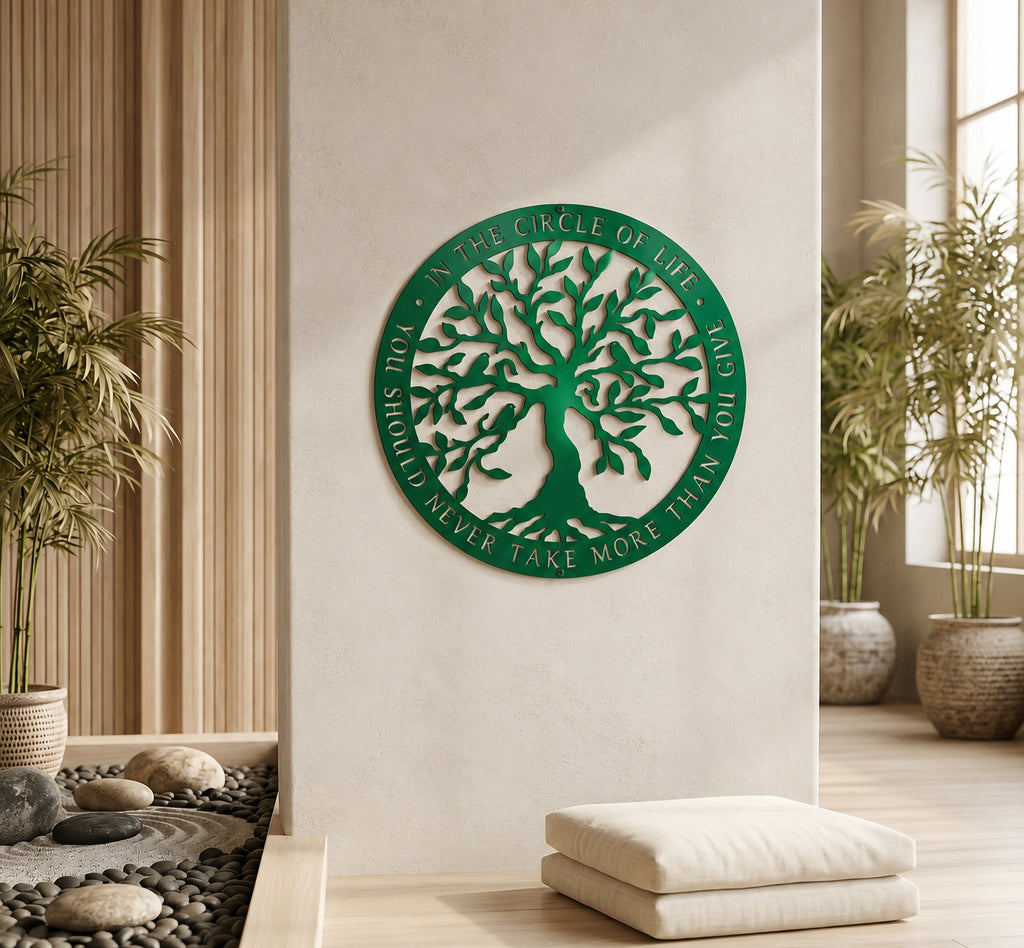 An emerald green circular metal sign showcasing a leafy tree with birds and the cut-out words "IN THE CIRCLE OF LIFE, YOU SHOULD NEVER TAKE MORE THAN YOU GIVE" around its rim. The sign hangs on a cream wall above stacked white meditation cushions in a serene room with potted palms and vertical wood paneling.