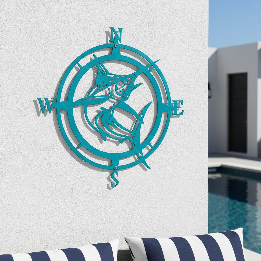 Bright turquoise blue marlin metal compass sign mounted on a textured white outdoor wall above a pool seating area with navy and white striped pillows.