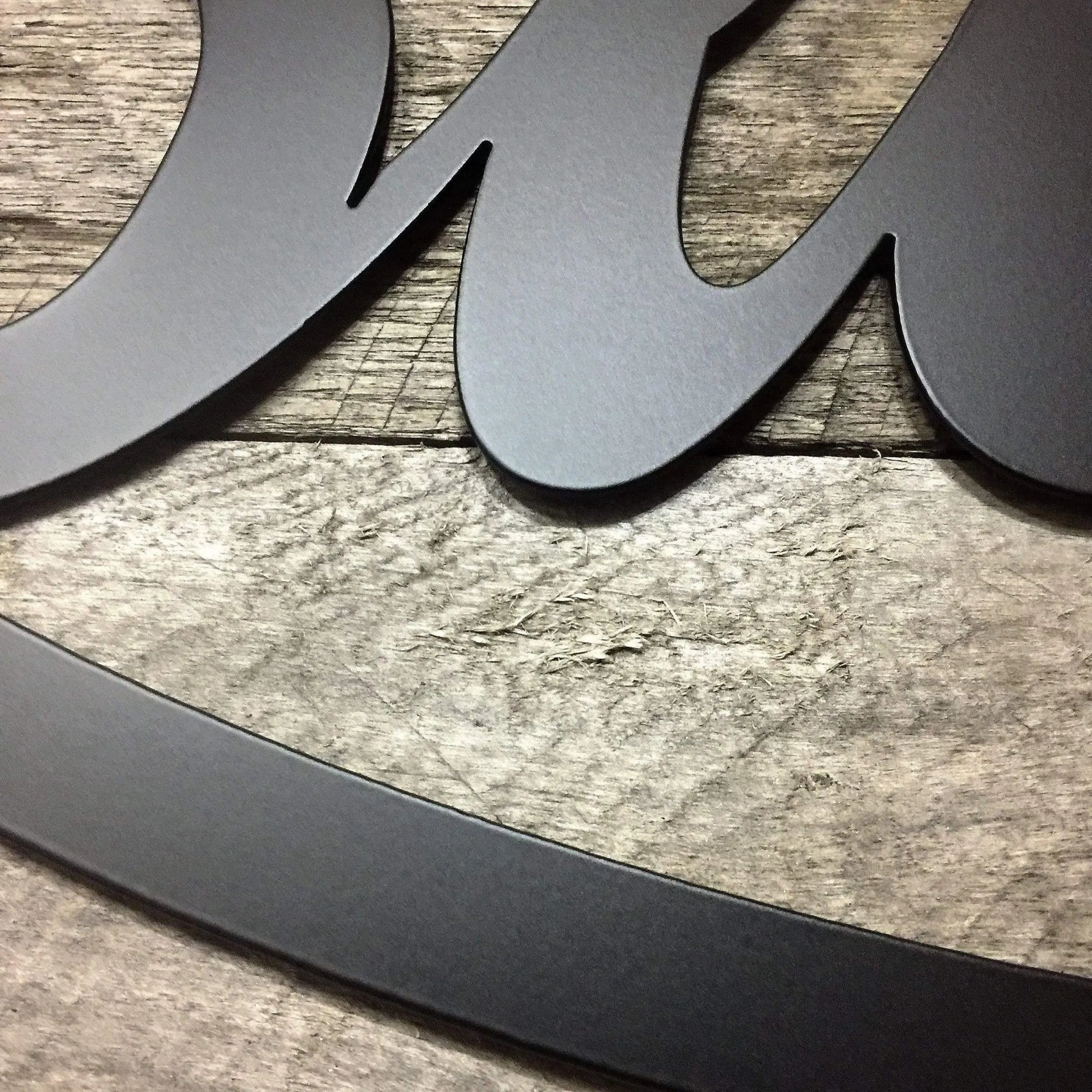 Close-up of a black metal Blessed Sign Established Sign - Personalized Family Name Sign, showcasing its elegant, laser-cut design on a wood surface, highlighting precision craftsmanship and durability.