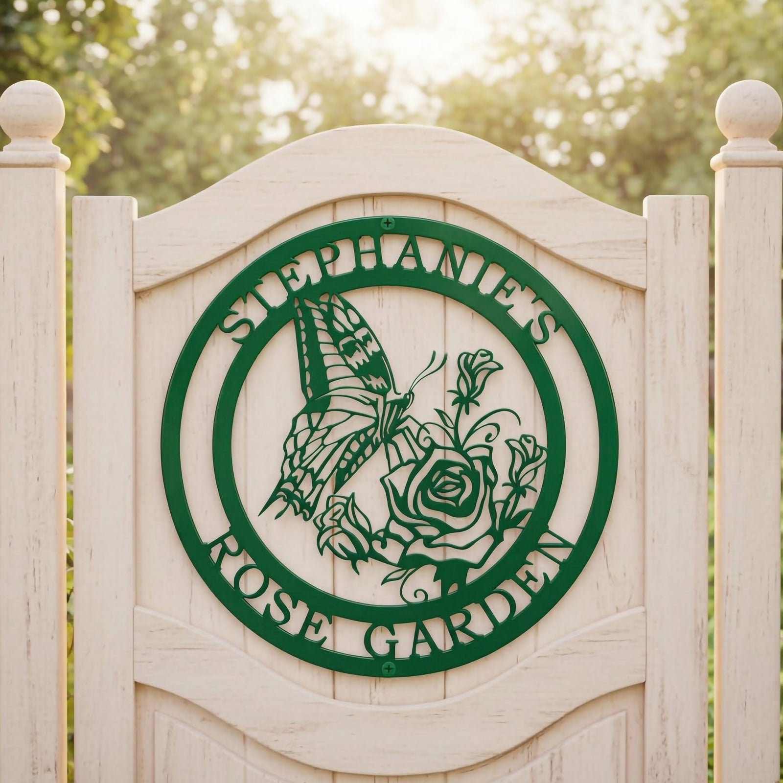 Emerald green custom metal round sign featuring a butterfly and rose cutout layout, displayed centrally on an outdoor white arched wooden gate with sunlit trees in the background.