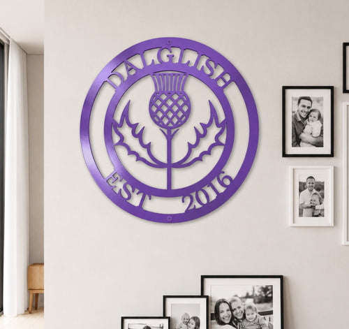 Bright lilac purple finish of the custom personalized Scottish thistle metal sign styled on a neutral-toned wall above a dark wood entryway credenza.